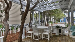 A covered outdoor seating area with white chairs and a table, surrounded by trees and a white fence. - Conch Cottage (Santa Rosa Beach)