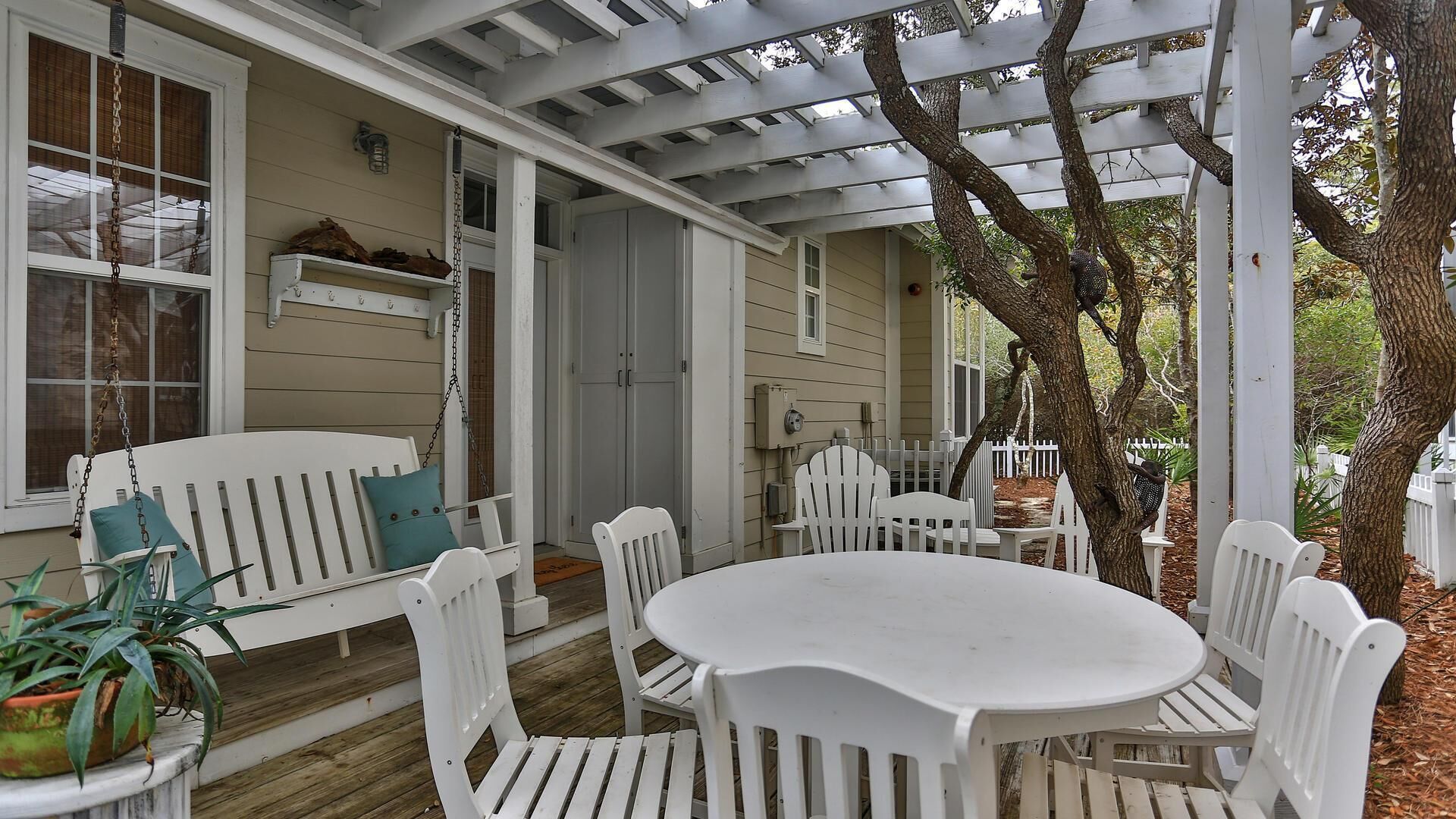 A covered porch with white wooden furniture, including a bench and a table with chairs.