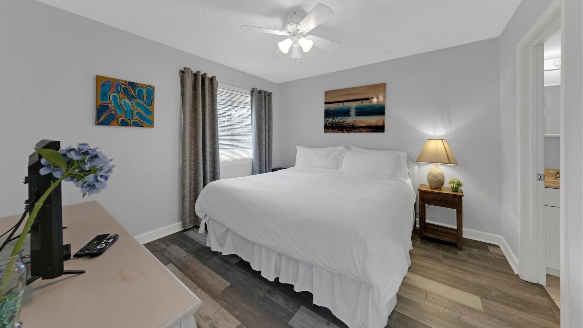 A hotel room with a bed, a desk with a computer, a lamp, and artwork on the walls.