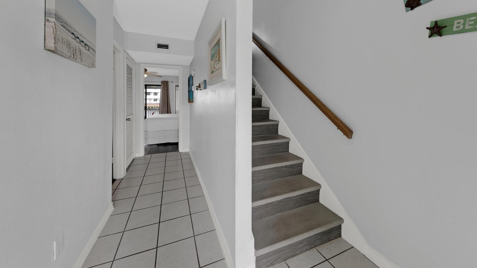 Ein Korridor mit Fliesenboden, der zu einer Treppe mit hölzernem Geländer führt.
