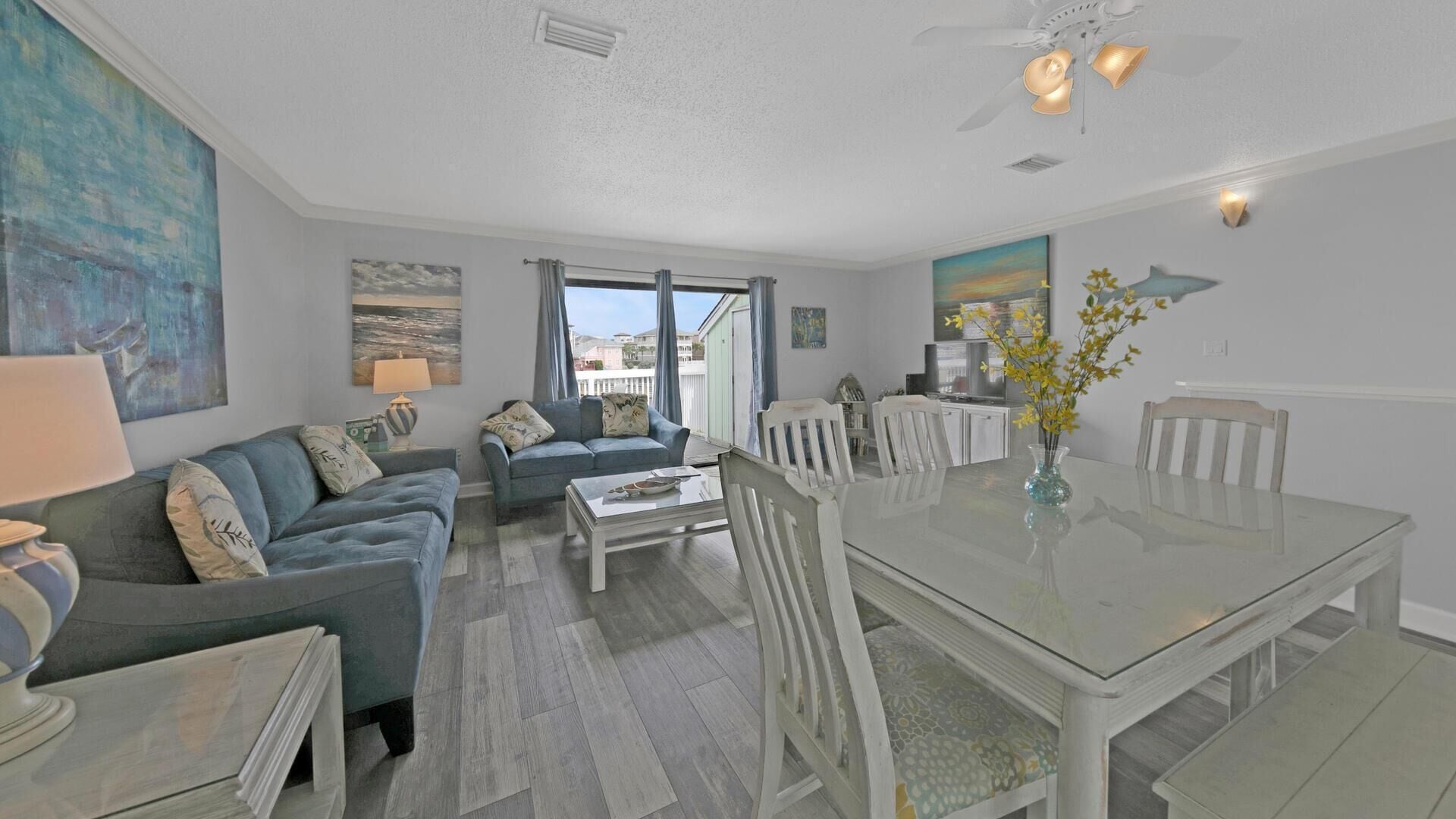 A spacious living area with a glass dining table, two sofas, and a ceiling fan.