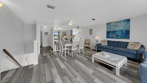 A spacious living room with a blue sofa, white dining table, and a kitchen in the background. - Southbay by the Gulf 60 (Destin)
