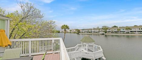 A waterfront property with a dock extending into a calm body of water, surrounded by residential buildings and lush greenery.