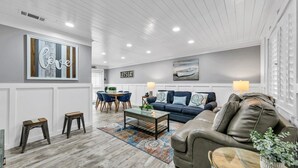 Un salon avec un canapé bleu, un divan en cuir marron, une table basse et un coin repas comprenant des chaises bleues et une table en bois.