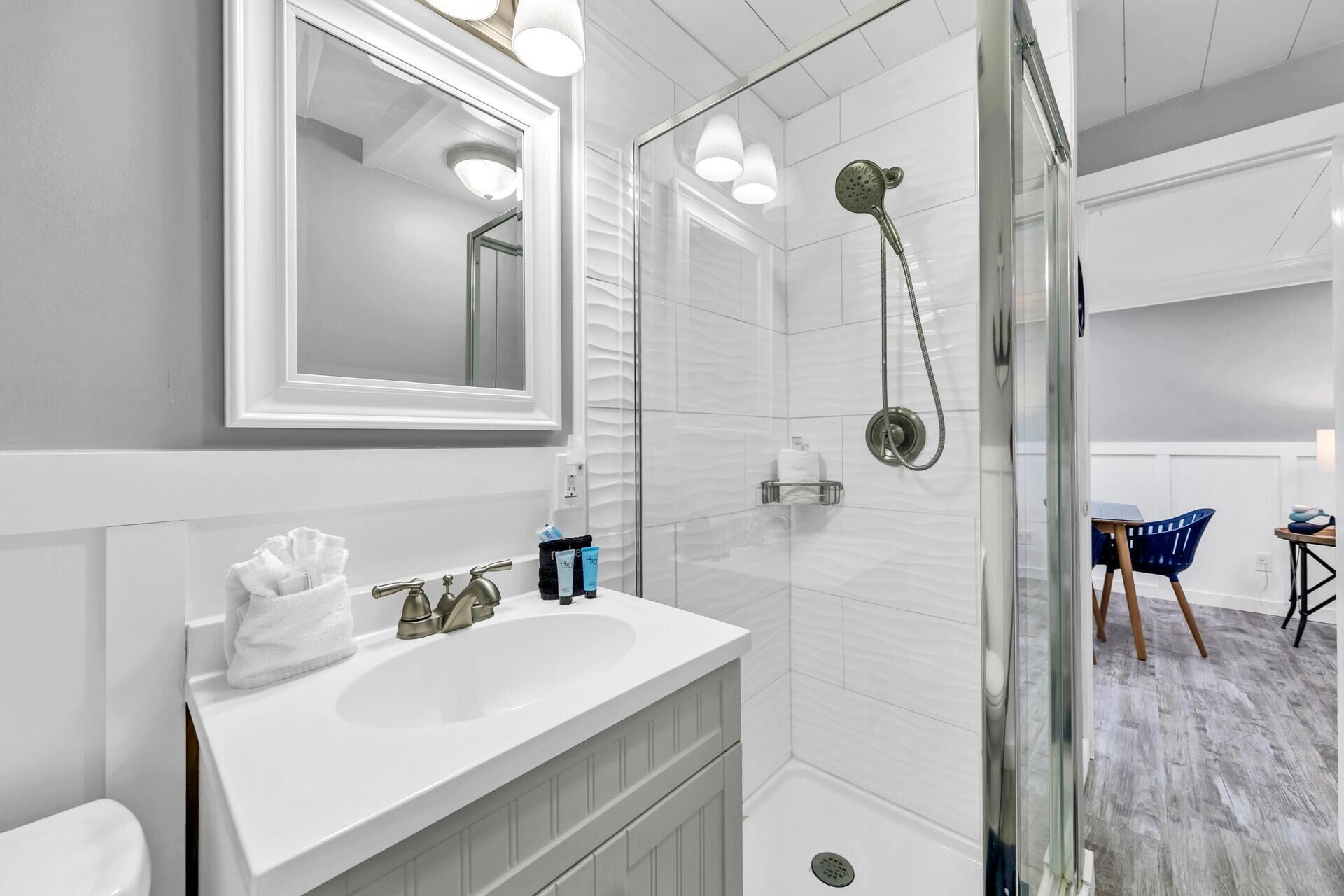 A modern bathroom with a white vanity, a glass shower enclosure, and a large mirror.