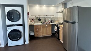 A compact kitchen with a washing machine, a stainless steel refrigerator, wooden cabinets, and a ceiling light fixture. - Furnished apartment in a great country setting. (Blythe)