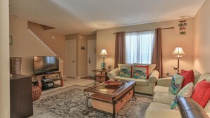 A living room with a sofa, TV, and two lamps. There's a staircase leading to another room. - Southbay by the Gulf 73 (Destin)