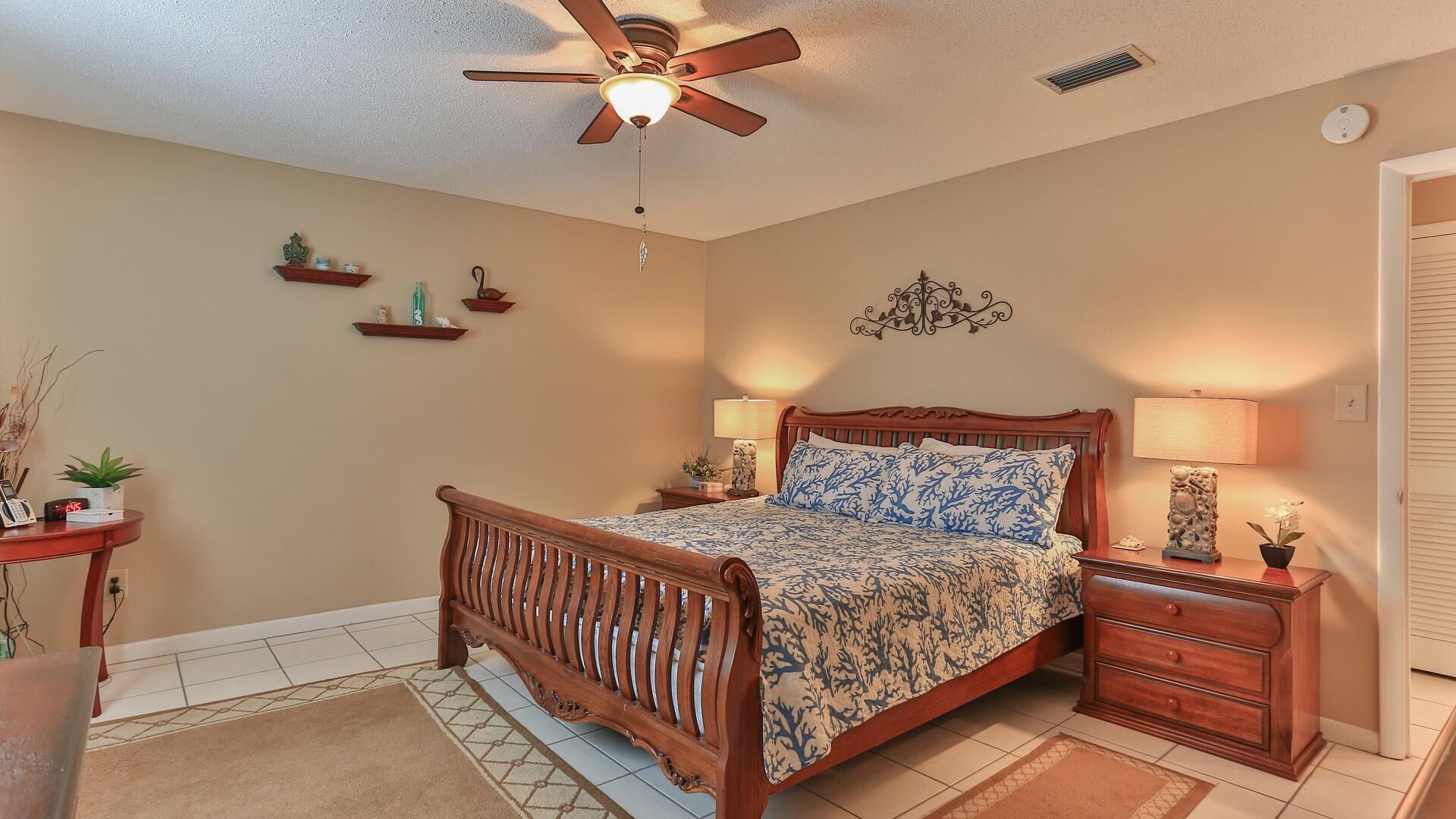 A bedroom with a wooden bed, bedside lamps, a ceiling fan, and decorative wall shelves.