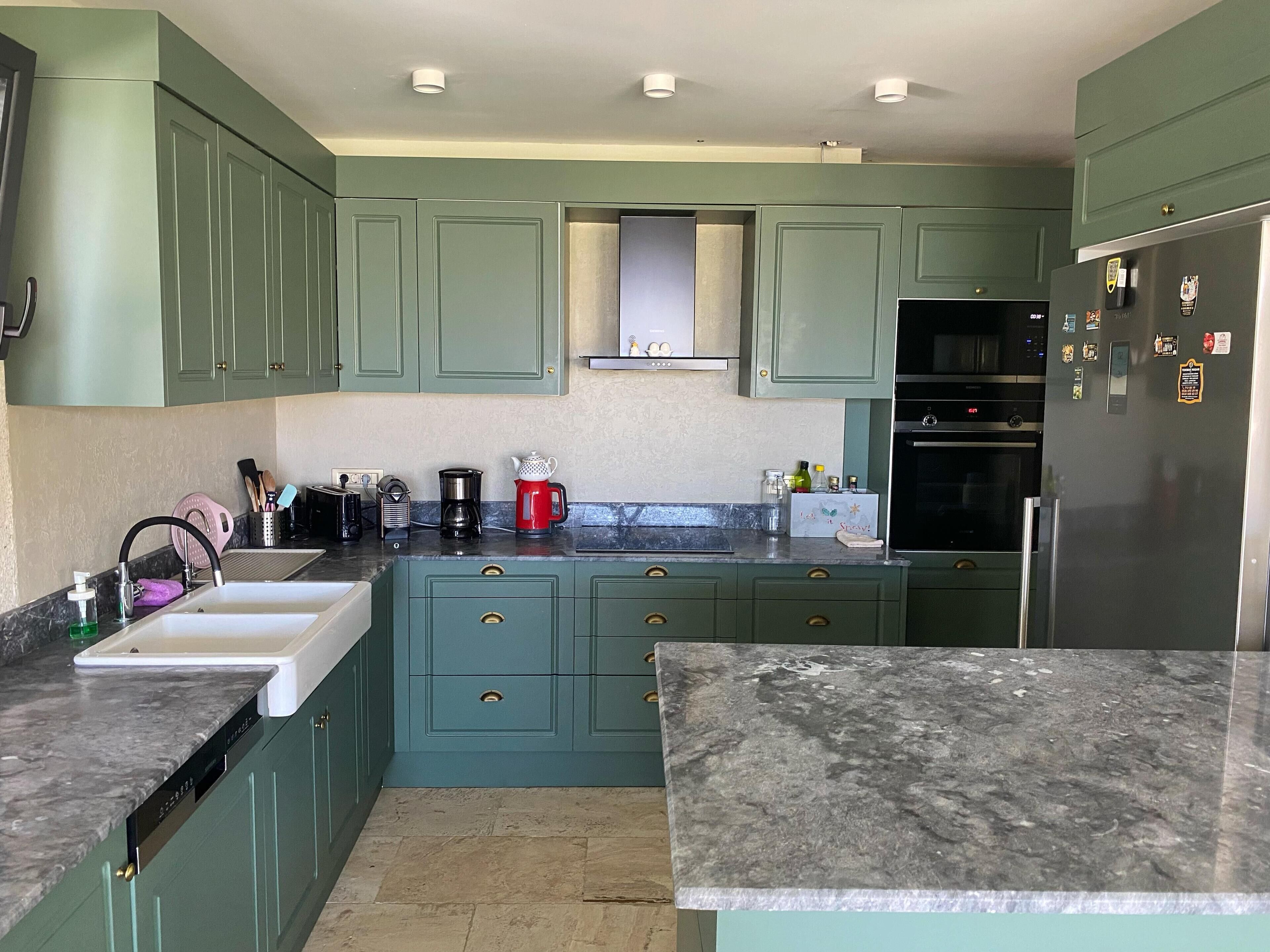 Una cocina con gabinetes color turquesa, encimera de granito, refrigerador de acero inoxidable y horno empotrado.