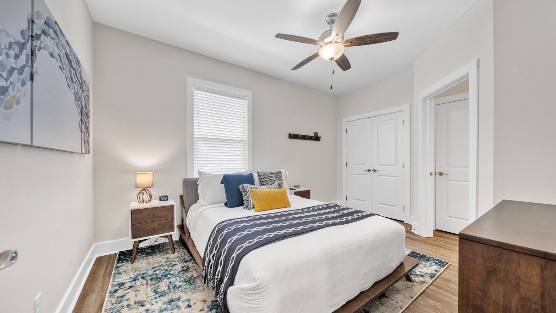 A bedroom with a bed, nightstand, lamp, ceiling fan, window, and wardrobe.