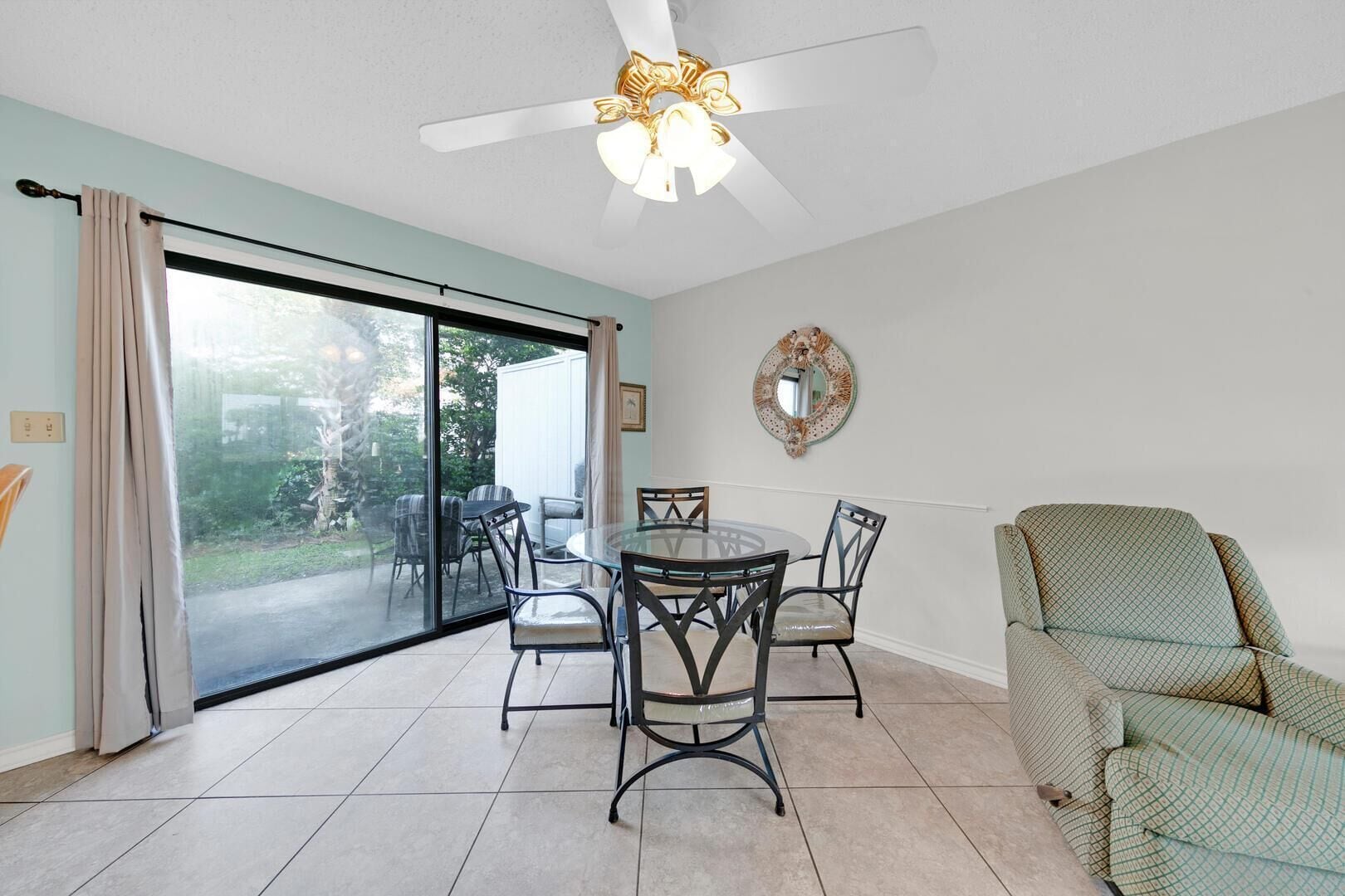 A dining area with a glass door leading to a patio, a ceiling fan, and a patterned armchair.
