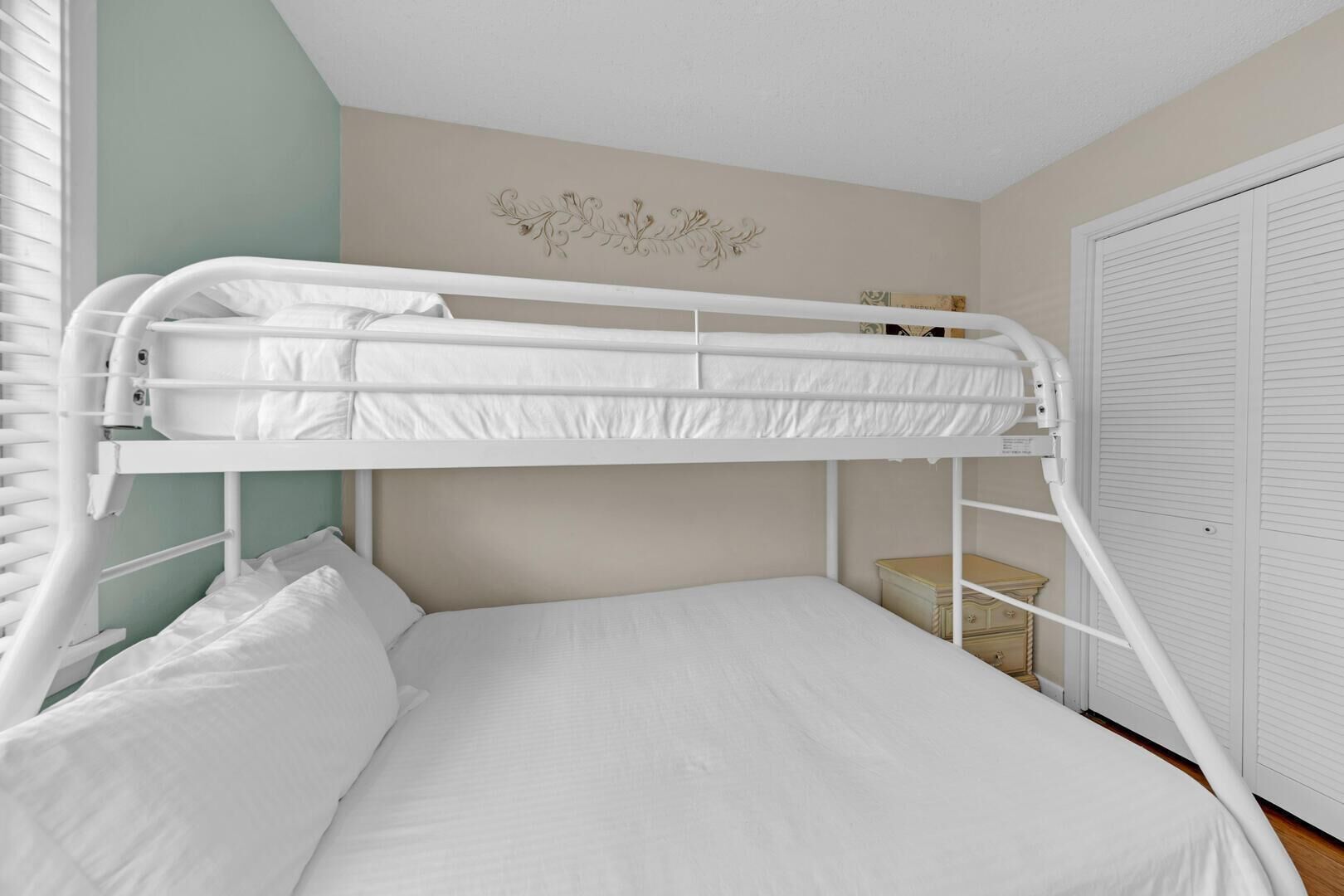 Una cama litera con ropa de cama blanca en una habitación con pared verde claro y puerta blanca.