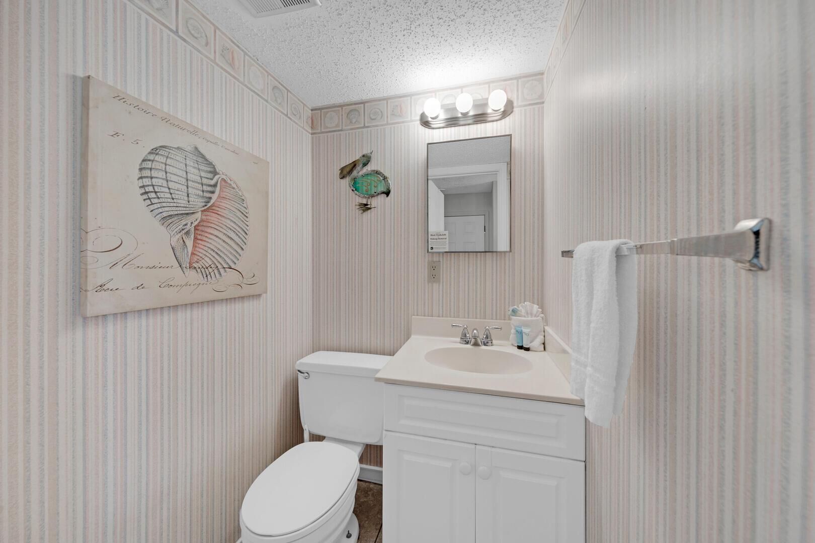 A bathroom with striped wallpaper, a white toilet, a sink with a mirror above it, and a towel rack.
