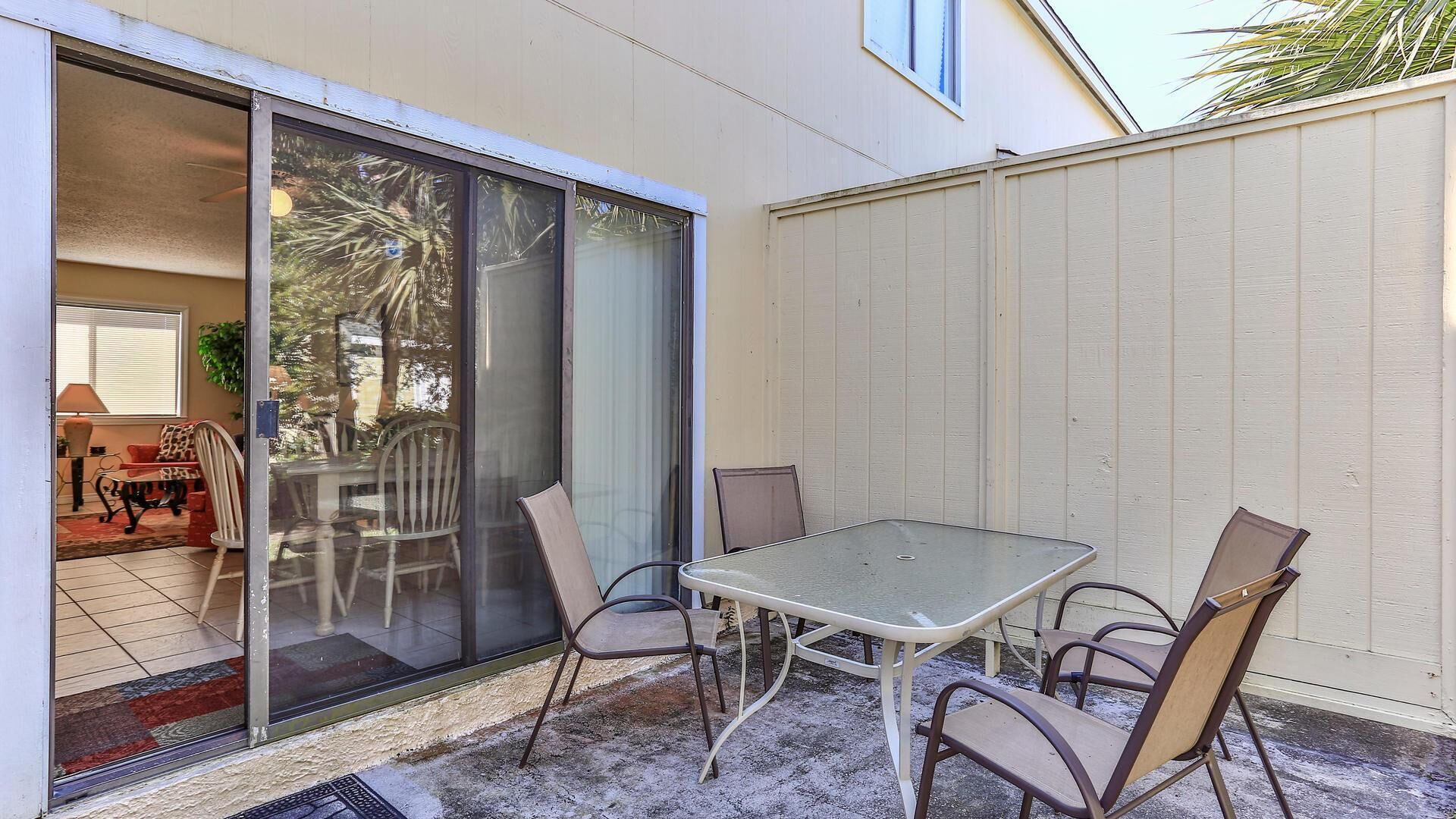 An outdoor patio with a table and chairs, a sliding glass door leading to a room, and a white fence.