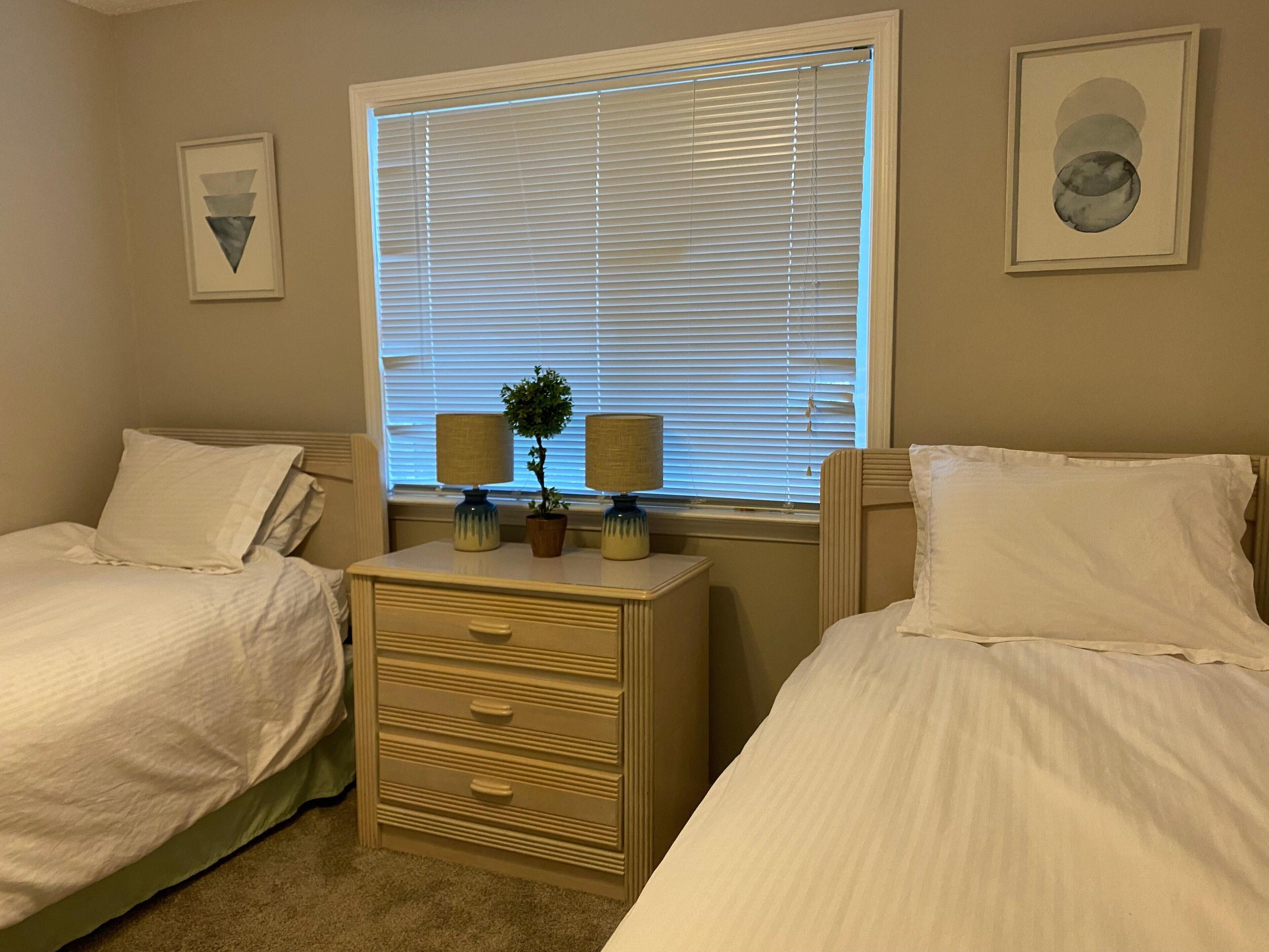 A bedroom with two beds, a dresser, and a window with blinds.