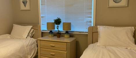A bedroom with two beds, a dresser, and a window with blinds.