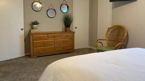 Een slaapkamer met een bed, een houten dressoir, een rieten stoel, een flatscreen-televisie aan de muur en drie spiegels.