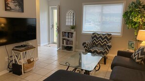 Een woonkamer met een flatscreen televisie, een boekenkast, een gestreept fauteuil, een glazen salontafel en een bank.