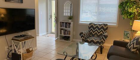A living room with a flat-screen TV, a bookshelf, a patterned armchair, a glass coffee table, and a sofa.