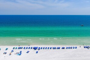 A beach with white sand and clear turquoise water. There are blue umbrellas and lounge chairs along the shore. - Southbay by the Gulf 99 (Destin)