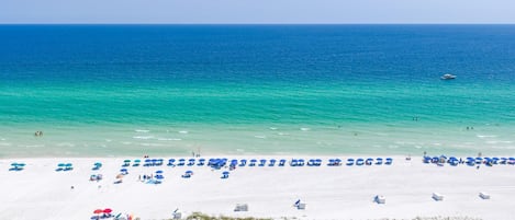 A beach with white sand, clear turquoise water, and a row of blue umbrellas.