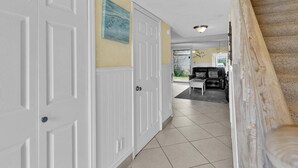 A hallway with white doors, a dining area with a black leather couch, and a staircase.