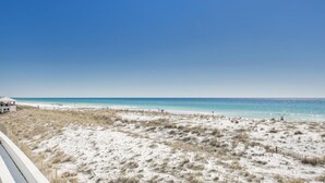 A beach with white sand, clear blue water, and a few people.