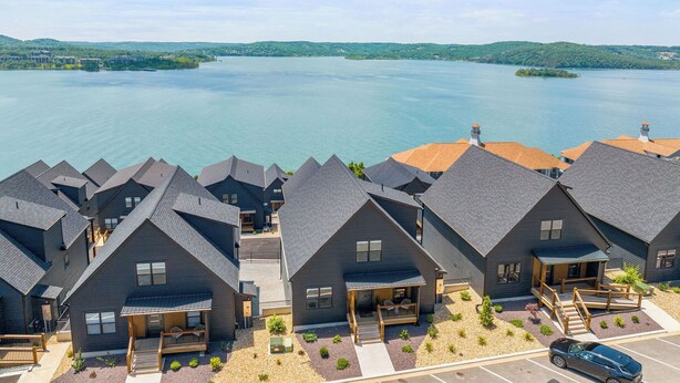 Un hôtel moderne composé de plusieurs bâtiments aux couleurs sombres, doté d’un parking et offrant une vue sur un grand lac.