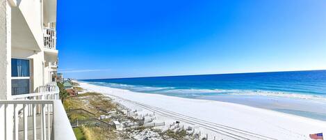A beach view from a balcony with a clear sky, a sandy beach, and a flag.
