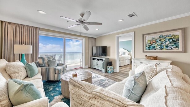 A spacious living room with a large window, a ceiling fan, a television, and a painting on the wall. - Crystal Dunes 405 (Destin)