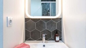 A modern bathroom with a white sink, a mirror with a light, and a hexagonal tile backsplash. - Central Part-Dieu - Apartment 2 - A/C available (Lyon)