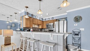 A modern kitchen with wooden cabinets, stainless steel appliances, and a bar area with stools. - Crystal Villas 6A (Destin)