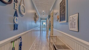 A hallway with a wooden floor, white wainscoting, and a view into a dining area. - Crystal Villas 6A (Destin)