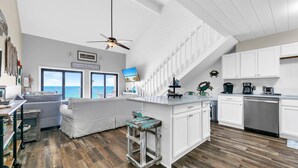 A modern kitchen with white cabinetry, a wooden floor, and a view of the ocean through large windows. - Crystal Villas 12B (Destin)