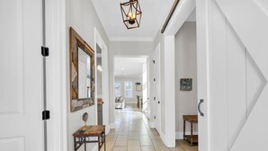 A hallway with white walls, a wooden bench, a mirror, and a hanging light fixture. - Wanderlust (Destin)