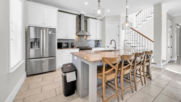 A modern kitchen with white cabinetry, stainless steel appliances, a granite countertop island, and a wooden dining set. - Wanderlust (Destin)