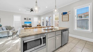 A modern kitchen with granite countertops, stainless steel appliances, and pendant lighting. - Wanderlust (Destin)