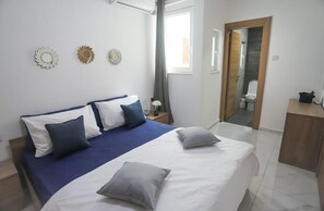 A bedroom with a bed, pillows, a nightstand, a mirror, and a bathroom visible through an open door. - Stunning 2 Bedroom, 2 Bathroom apt St Julians (St. Julian's)