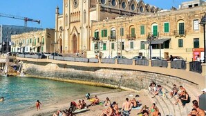 A coastal scene with a historic church, a promenade, and people sunbathing on the beach. - Stunning 2 Bedroom, 2 Bathroom apt St Julians (St. Julian's)