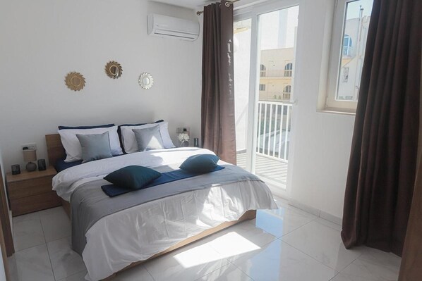 A bedroom with a bed, nightstands, and a view of a balcony.