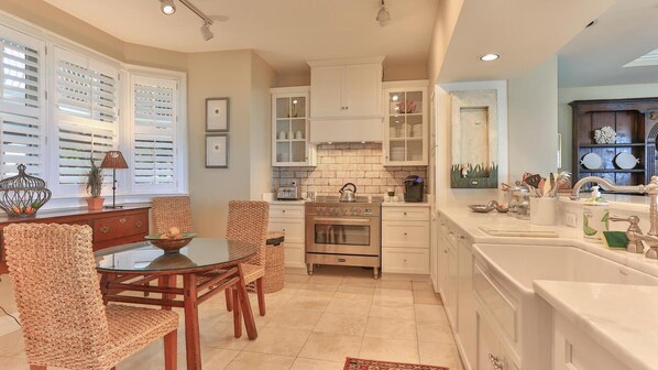 A modern kitchen with white cabinetry, a built-in oven, and a dining area with wicker chairs and a glass table. - Grandview 102 (Miramar Beach)