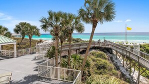 A wooden boardwalk leading to a beach with palm trees and a clear blue sky. - Hidden Dunes Gulfside 206 (Miramar Beach)