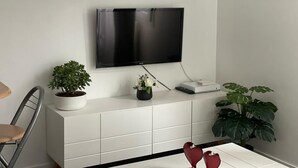 A modern living room with a flat-screen TV mounted on a white cabinet, a dining table with chairs, and a potted plant. - Paris15/parc des Expositions/Issy-les-Moulineaux  (Issy-les-Moulineaux)