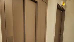 A hallway with beige walls and a brown floor, leading to a door with a visible light switch and a small sign above it. - Paris15/parc des Expositions/Issy-les-Moulineaux  (Issy-les-Moulineaux)