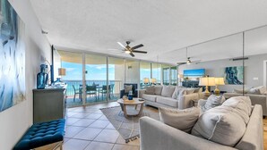 A spacious living room with a large sofa, a coffee table, and a TV. There is a balcony with a view of the ocean. - Hidden Dunes Gulfside 502 (Miramar Beach)