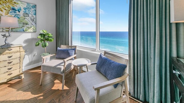 A room with a view of the ocean, a wooden dresser, two chairs, a small table, and a lamp. - Leeward Key 1103 (Miramar Beach)