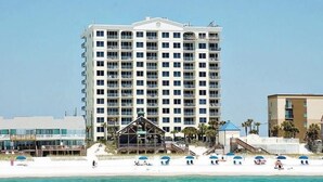A multi-story hotel with balconies, located near a beach with umbrellas and a pool area. - Leeward Key 1103 (Miramar Beach)