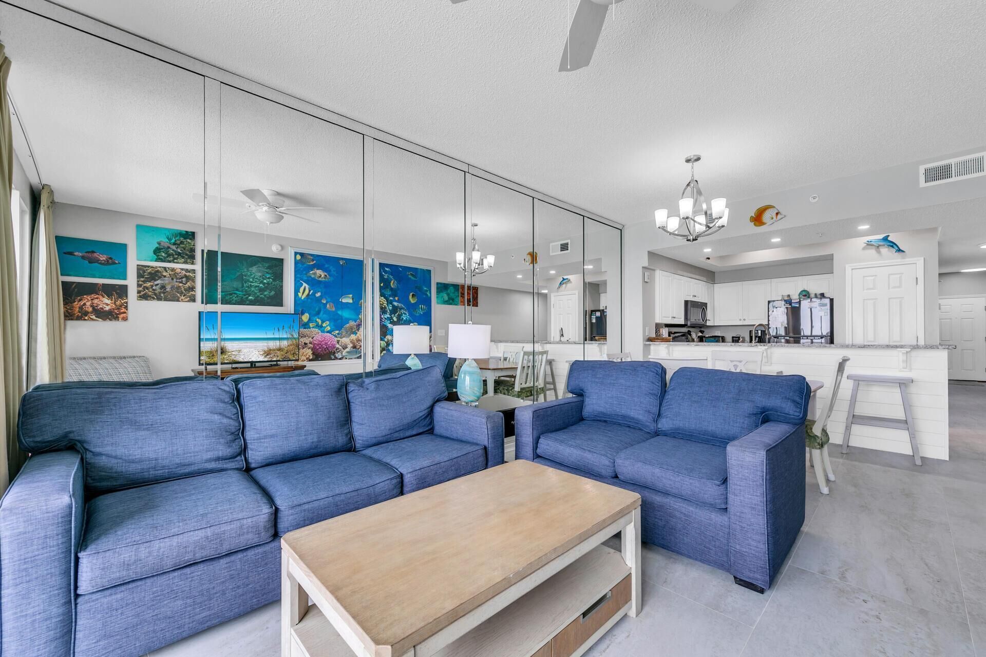 A modern living room with a blue sofa set, a wooden coffee table, and a kitchen in the background.