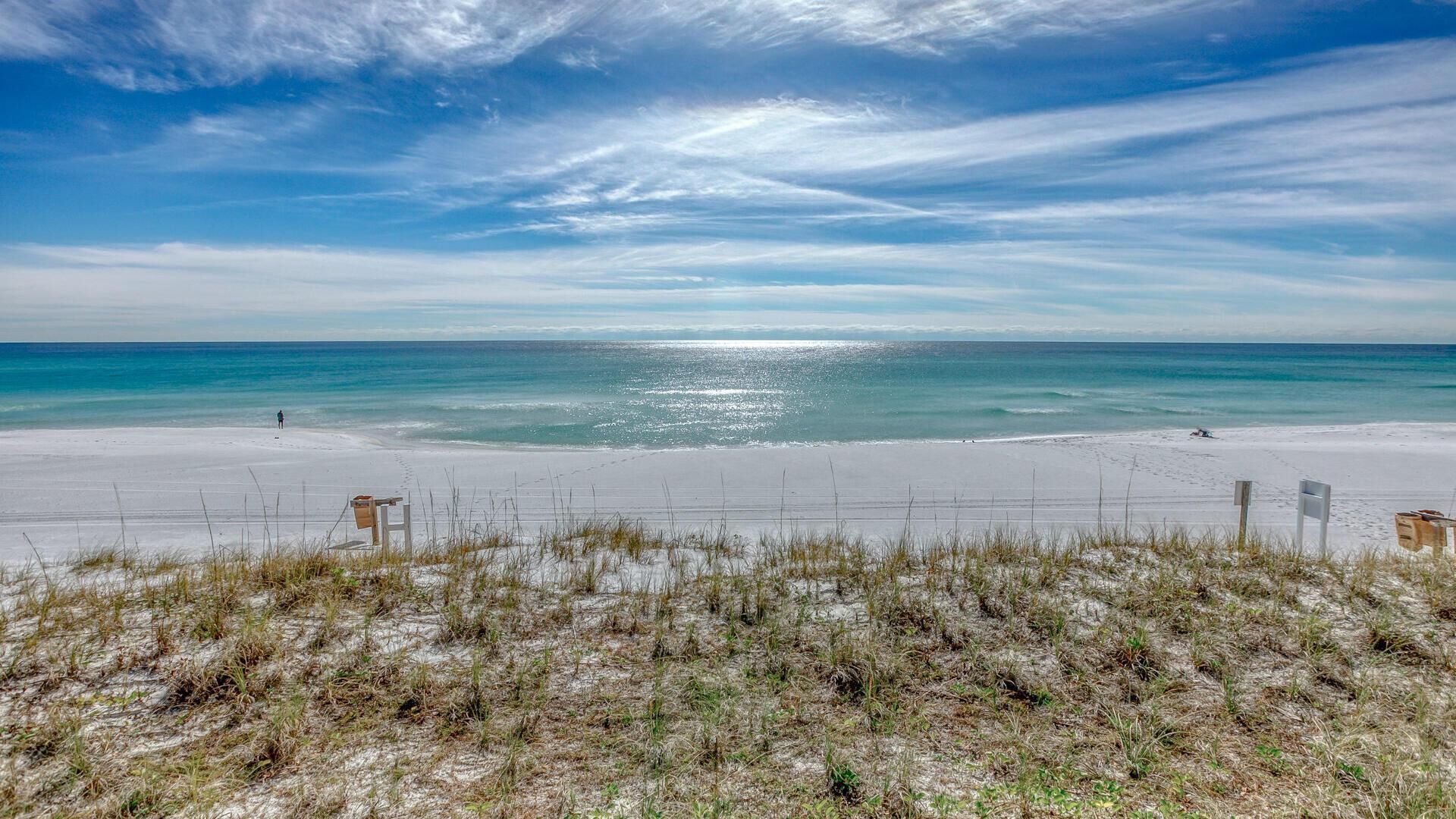Una playa con una valla y señalizaciones, cielo despejado y el océano.