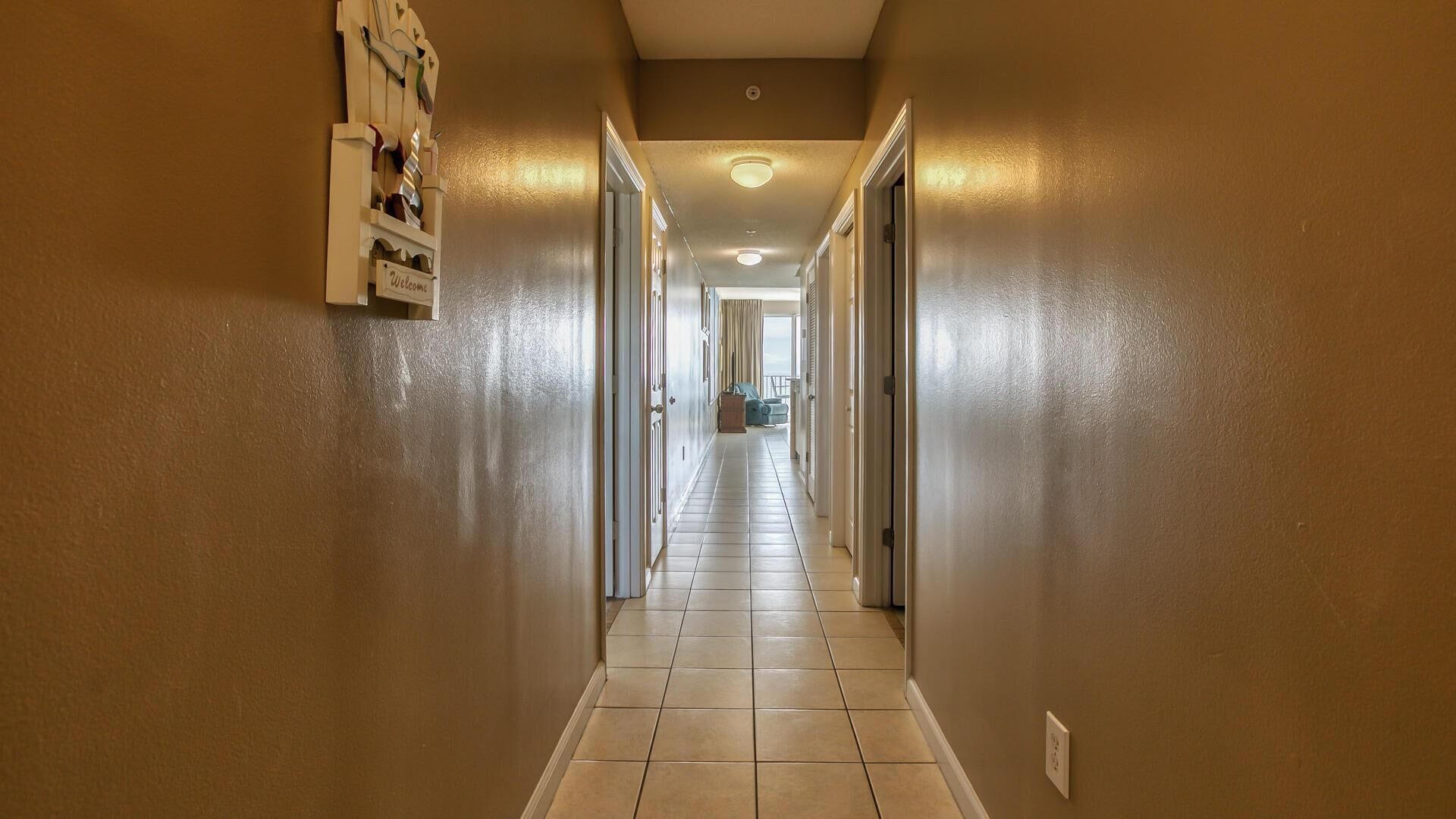 A hallway with a 'Welcome' sign, doors on both sides, and a view into a room with a blue chair.